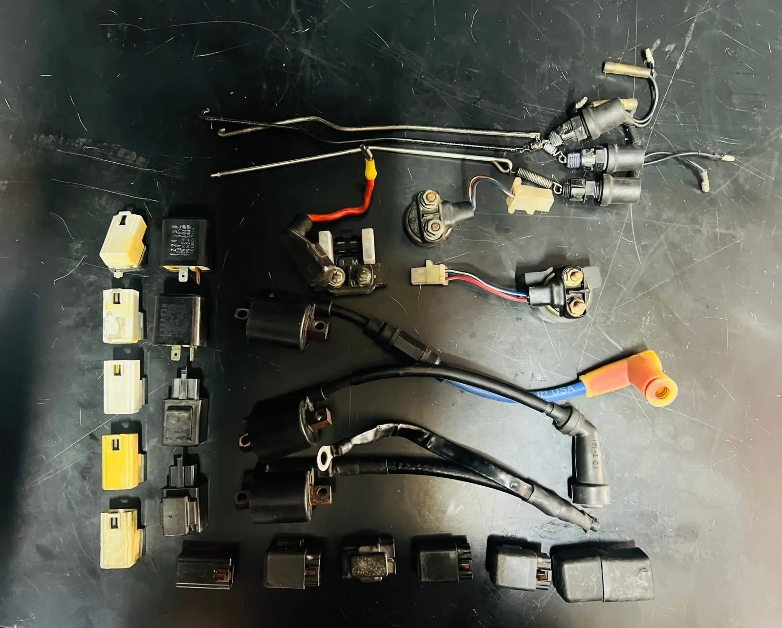 Motorcycle ignition and electrical parts organized on a dark surface